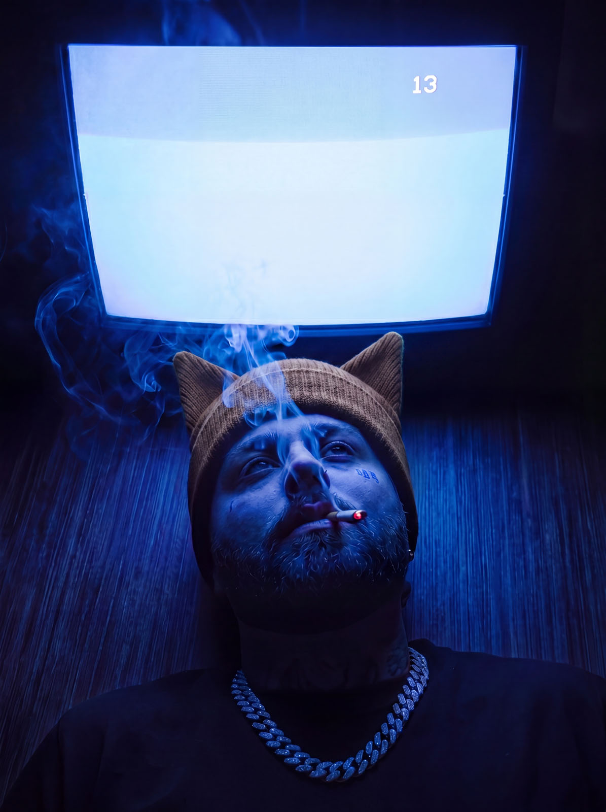 Blue-lit portrait with a smoking figure wearing a cat-ear beanie under a CRT screen